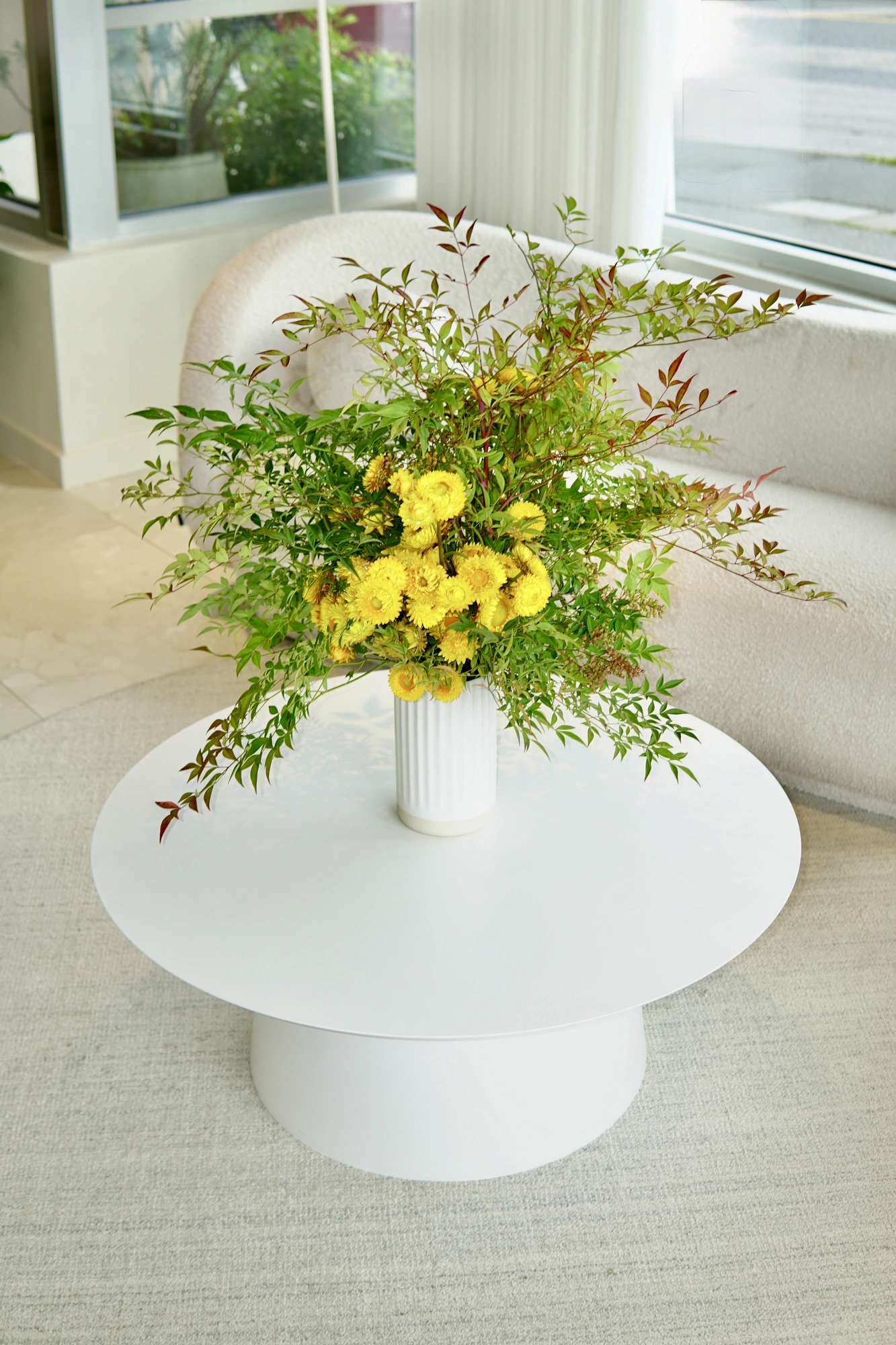 Yellow strawflowers and nandina in a fluted white vase