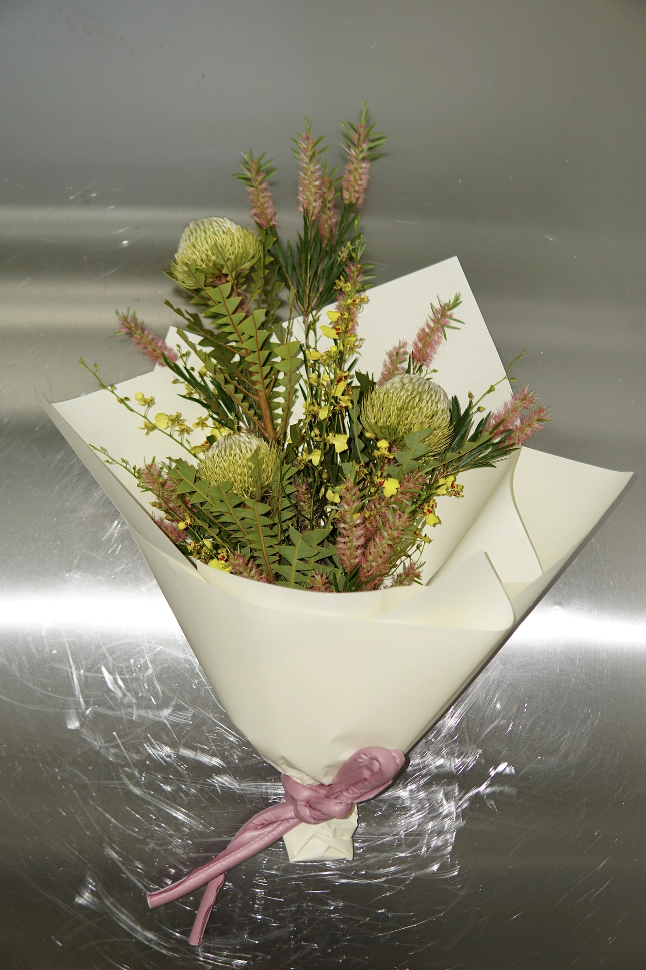 Protea, banksia foliage, and pink veronica in a hand-tied wrap