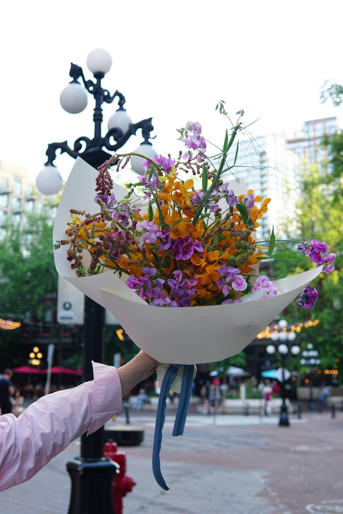 Hand-tied bouquet of sweet pea and orange bloom, wrapped in white paper on a Vancouver street