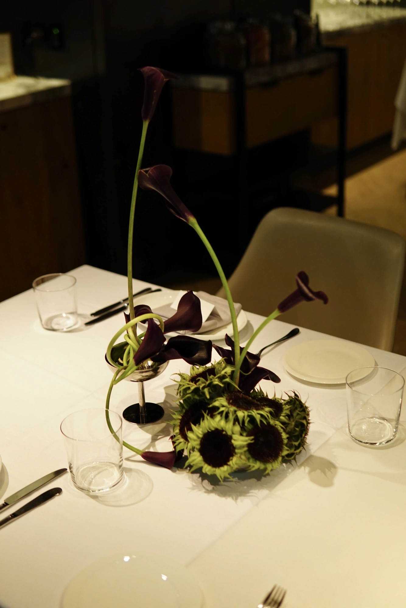 Close study of sunflower heads and aubergine calla lilies in a steel cup