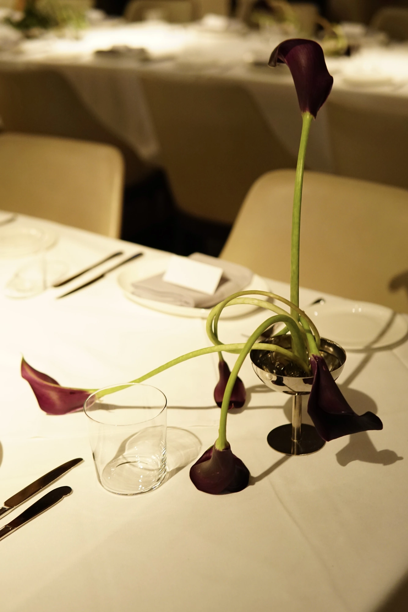 Low calla lily centrepiece with stems spilling across a white tablecloth