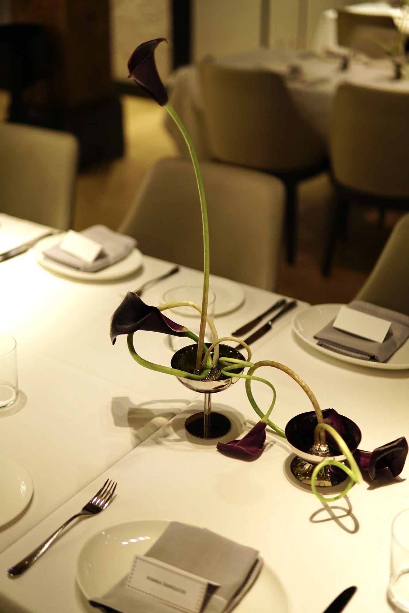 Two steel cups of dark calla lilies along a wedding dining table